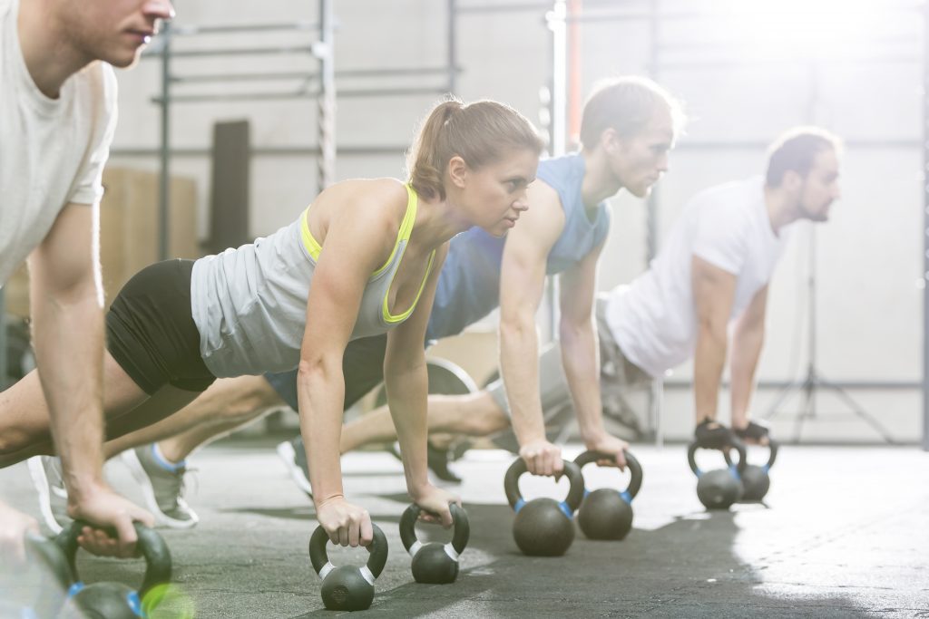 Determined people doing pushups with kettlebells at crossfit gym